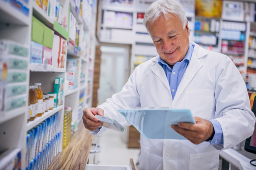 Male pharmacist checking medicine on clipboard at the drugstore.