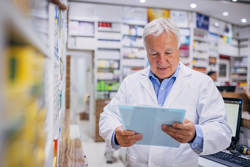 Male pharmacist checking medicine on clipboard at the drugstore.
