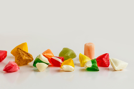 Large group of all sort of multicolored candies spilling out from a glass jar shot from above on yellow background. High resolution 42Mp studio digital capture taken with SONY A7rII and Zeiss Batis 40mm F2.0 CF lens