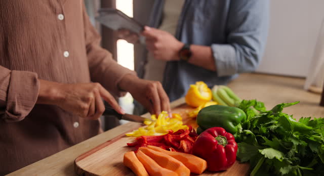Person, hand and chopping vegetables on board for healthy nutrition salad or dinner, carrots or pepper. Chef, helper and tablet for online recipe in kitchen for prepare ingredients, cook or wellbeing