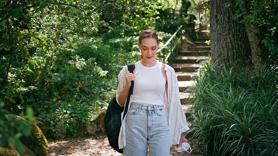 Adventurous girl walking forest trail summer weekend close up. Attractive carefree woman with backpack going on nature relaxing sunny morning. Happy calm female tourist looking camera enjoying leisure