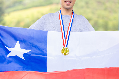 Triumphant Chilean male athlete proudly showcases a gold medal, symbolizing victory. Holding the Chilean flag, he embodies national pride during sporting events