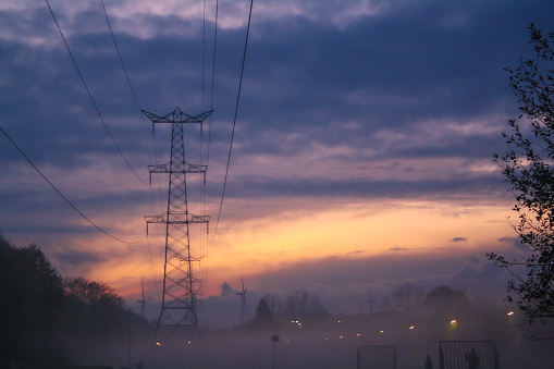 Foggy sunset over a playfield in a residential area of ‘s-Hertogenbosch (den bosch), located in the province of North Brabant. In the foreground is a transmission tower and all the way in the background are some windturbines. Also there are 2 people, in silhouette, playing soccer
