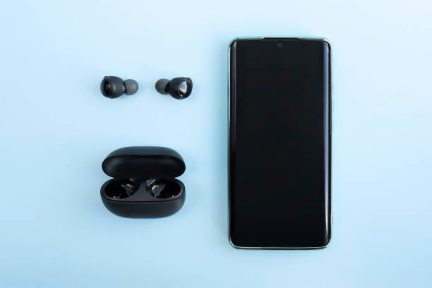 istock Smartphone and wireless headphones or earbuds with charging case on bright blue background. Music technology. top view 1976186779