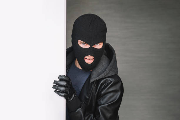 istock the thief looks out from around corner, copy space. thug keeps the front door Maniac broke into the room. the thief broke down the door. The evil look of the bandit on the camera. dangerous guest 1976187789