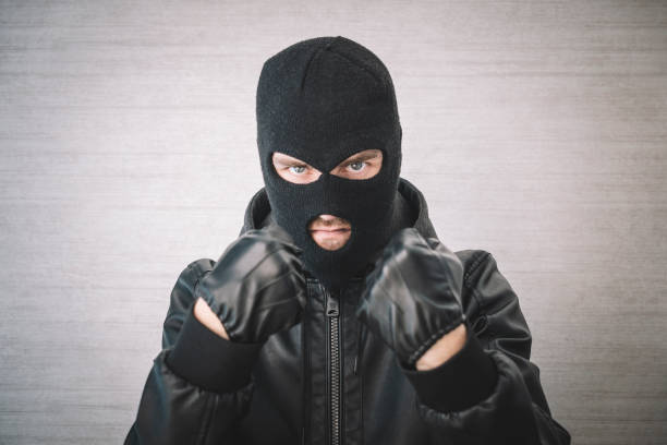 istock thief in a black jacket. A man in a black balaclava with an evil expression on his face. An aggressive bandit on a white background. The concept of crime or theft. 1976187792