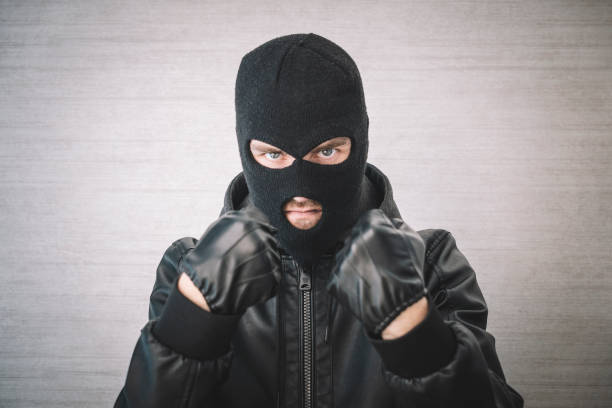 thief in a black jacket. A man in a black balaclava with an evil expression on his face. An aggressive bandit on a white background. The concept of crime or theft. A thief in a black jacket. A man in a black balaclava with an evil expression on his face. An aggressive bandit on a white background. The concept of crime or theft. wrongdoer stock pictures, royalty-free photos & images