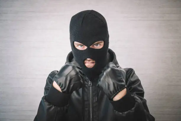 Photo of thief in a black jacket. A man in a black balaclava with an evil expression on his face. An aggressive bandit on a white background. The concept of crime or theft.