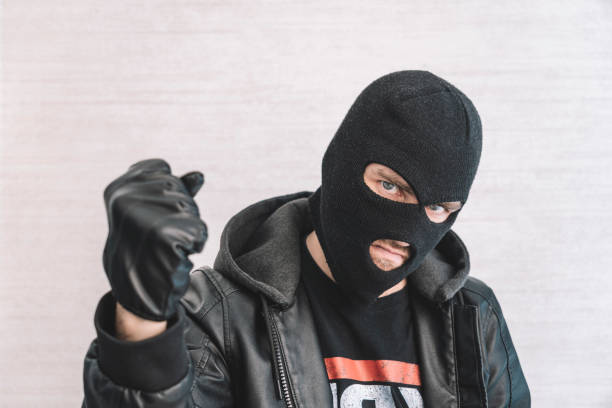 istock thief in a black jacket. A man in a black balaclava with an evil expression on his face. An aggressive bandit on a white background. The concept of crime or theft. 1976187794