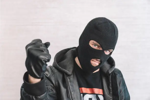 Photo of thief in a black jacket. A man in a black balaclava with an evil expression on his face. An aggressive bandit on a white background. The concept of crime or theft.