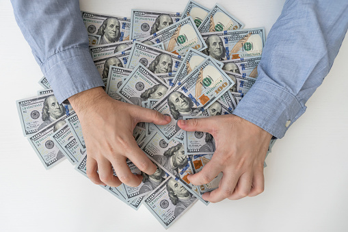 Man's hands and a lot of dollar bills on a white wooden table. Bribes, corrupt, cash. US dollars in male hands. The concept of profit, wages.