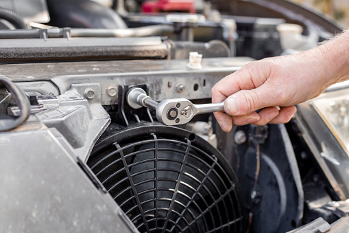 A man fixes an engine cooling fan under the radiator grill of a car. Machine maintenance and repair.