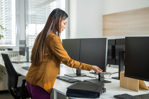 Asian woman turning off computer monitor after finishing working day in office