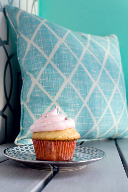 Pink Frosted Cupcake and Blue Pillow on Wood Surface with a Stylish Blue Wall