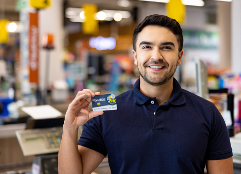 Happy Latin American cashier holding a loyalty card at a supermarket and looking at the camera smiling