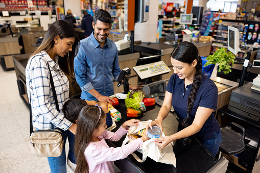Latin American family shopping at the supermarket and cashier helping them pack in a tote bag
