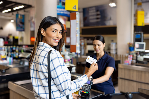 Happy Latin American woman paying at the supermarket using her credit card