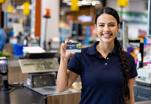 Happy Latin American cashier holding a loyalty card at a supermarket and looking at the camera smiling