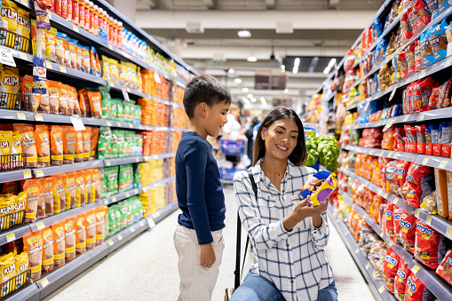 Latin American mother grocery shopping with her son at the supermarket and letting him chose a treat