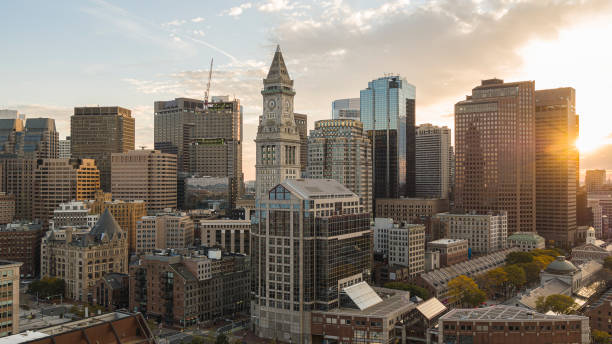 Financial district of Boston, Massachusetts. Skyscrapers skyline with famous Custom House Clock Tower and Faneuil Hall in the evening with visible sunbeam. Boston city skyscrapers with historic Custom House Clock Tower at the backdrop and Faneuil Hall Marketplace at the front. solar panels on the roof of building in a city stock pictures, royalty-free photos & images