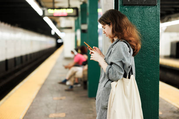 Young woman using smartphone on a platform of subway train station. Focus on foreground