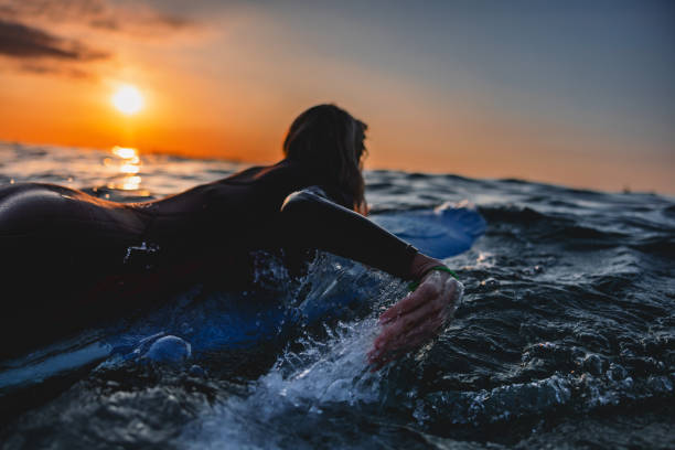 istock Back View Of A Female Surfer Paddling On Surfboard During A Sunset Surf Session 1976230480