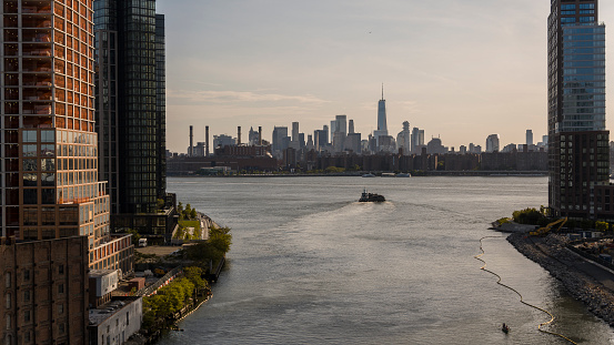 Lower Manhattan with Freedom Tower panoramic view from the Newtown Creek River in Greenpoint, Brooklyn. Tugboat is pulling a barge with scrap metal along the river.