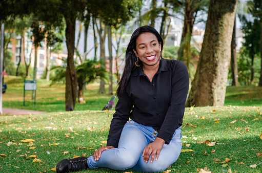 portrait of confident black woman dressing casual clothes sitting on grass in public park