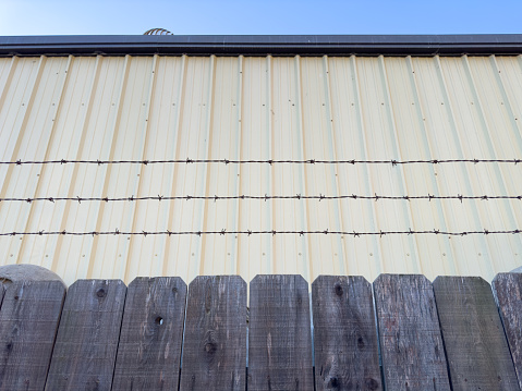 a warehouse fence barbed wire fencing commercial building industry industrial facility storage alleyway alley safety concept private sharp security metal zone closeup factory architecture yard wall