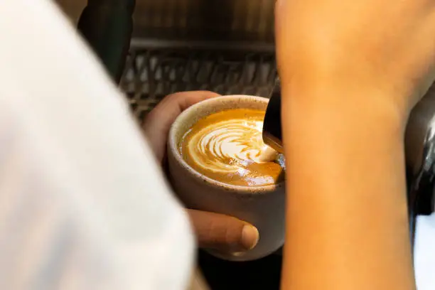 Barista making latte art in a white cup, adding a creative touch to your coffee.