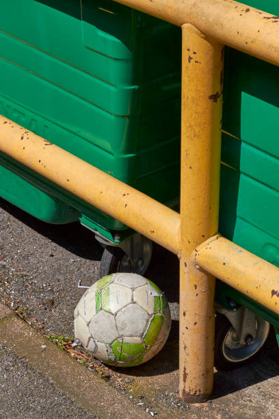 A worn down white soccer ball is seen discarded beside a rubbish bin.