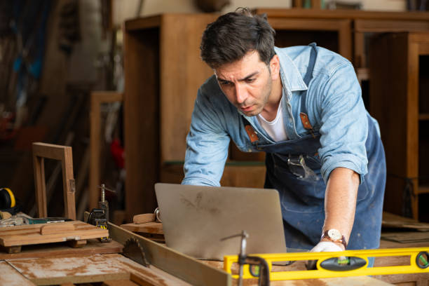 istock Carpenter working on laptop in his workshop at a woodworking factory 1976554356