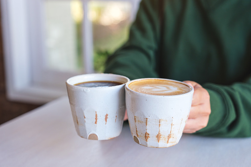 Closeup image of a woman holding and serving two cups of hot coffee