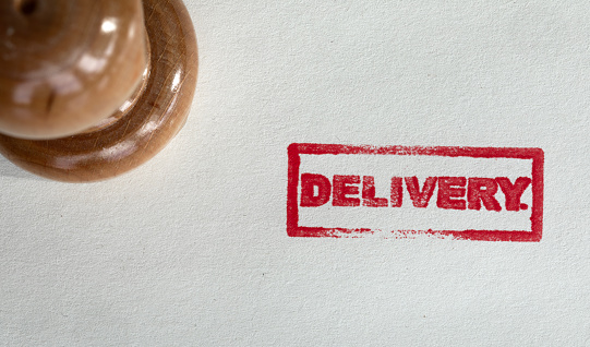 Wooden delivery stamp on white textured paper. Horizontal composition with copy space. Directly above view.