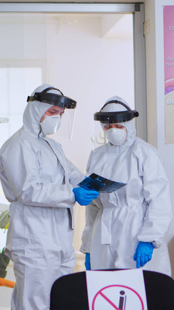 istock Dental doctors with protection suit analysing teeth x-ray in reception 1976693414