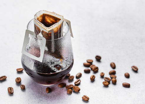 A  glass of freshly brewed drip coffee.  Drip coffee bag with ground coffee for brewing in a glass