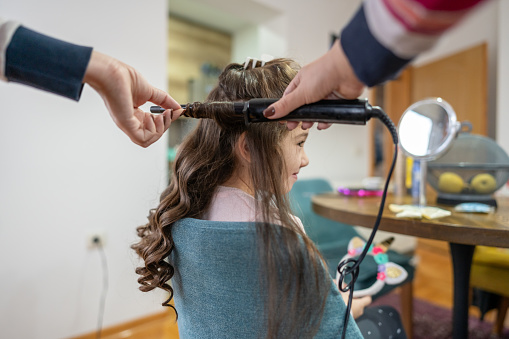 Mother making hair curls to daughter with straightening iron