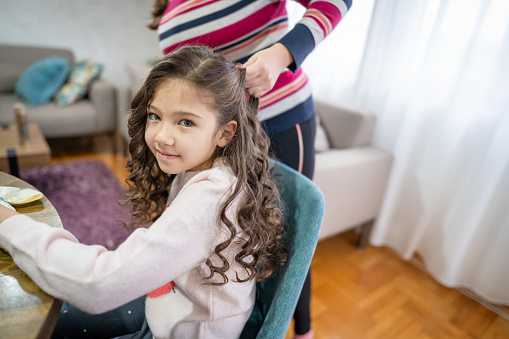 Mother making hair curls to daughter with straightening iron