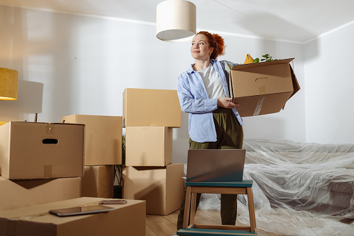 Smiling beautiful woman holding cardboard box in new apartment