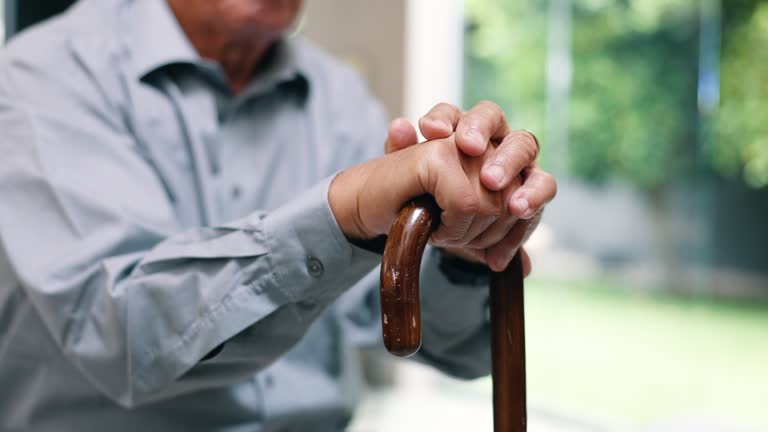 Hands, senior person and walking stick in closeup for recovery, balance and rehabilitation in nursing home. Retirement, wood cane and mobility aid for steps, movement and zoom on fingers in house