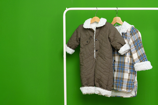 Two kids winter coats hanging on hangers against green wall in studio close up