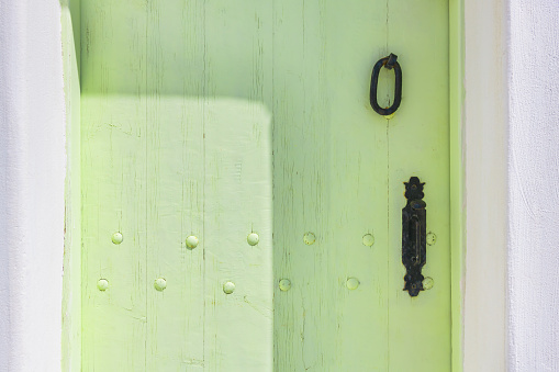 Green-painted vintage wooden door with metal handle close up. Cycladic architecture in Santorini island, Greece.