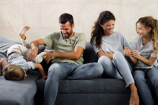 Cheerful parents and their small kids having fun on sofa in the living room.
