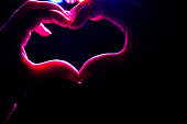 Female hands in the shape of a heart on a dark background, let in bright rays. Hands in the shape of a love heart. Valentine's day