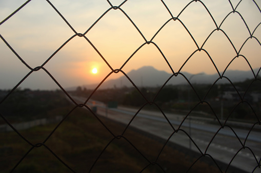The background of the sunset is behind the fence