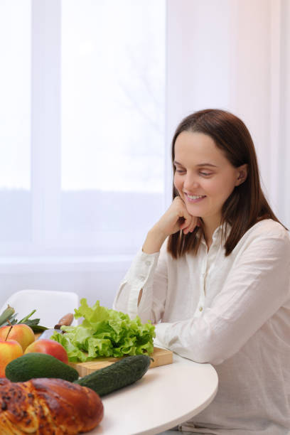 istock Caucasian brown haired woman sitting at kitchen table with fruit and vegetables having ingredients delightful and nutritious dish holding chin enjoying cooking and healthy nutrition 1976933627
