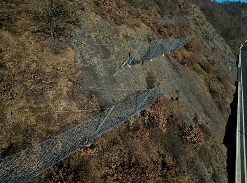 reinforcing slope with a steel net anchored deep into rock. rows inclined fences with massive netting above mountain pass will hold back large eroding boulders and falling stone, steel frame, circle, boulder, anchoring, screwed, stabilization