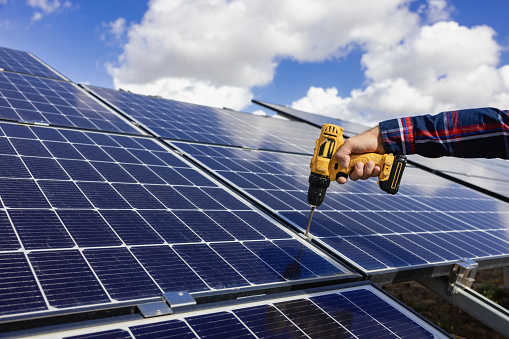 Worker using a power drill to work on a solar panel