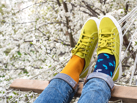 Trendy sneakers and colorful socks on the background of flowering trees. Closeup, outdoors. Men's and women's fashion style. Beauty and elegance concept