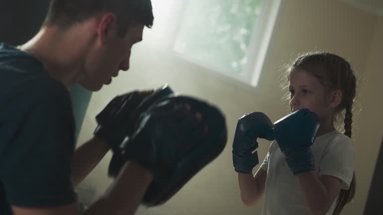 Trainer with pads and punching girl child in gym